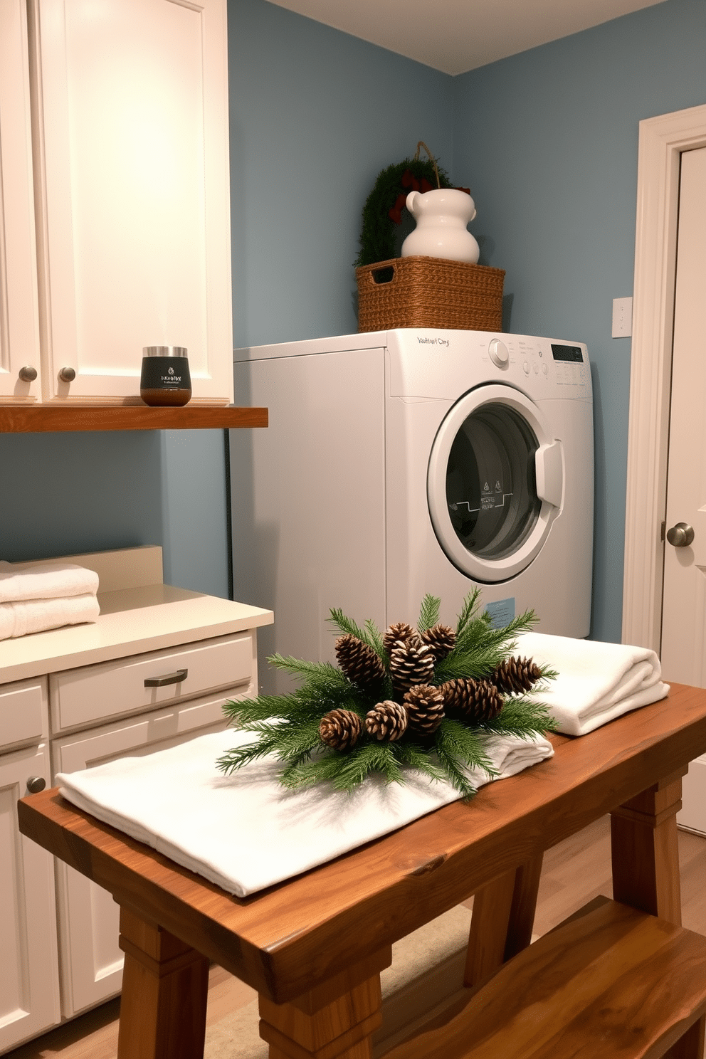 A cozy laundry room designed for winter ambiance. An aromatherapy diffuser sits on a wooden shelf, exuding soothing winter scents like pine and cinnamon. The walls are painted in a soft blue hue, complemented by white cabinetry. A rustic wooden table is adorned with neatly folded towels and a seasonal centerpiece of pinecones and evergreen branches.