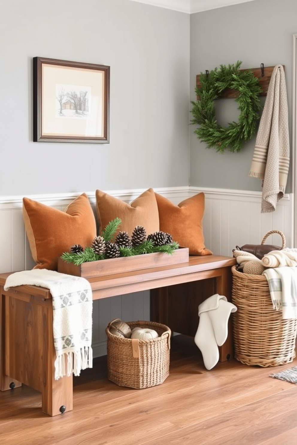 A cozy winter mudroom features a rustic bench made of reclaimed wood, adorned with plush cushions in earthy tones. Pinecone and evergreen centerpieces are artfully arranged on a wooden table, bringing a touch of nature indoors. The walls are painted in a soft gray, complemented by white wainscoting for a fresh yet inviting look. A woven basket sits beside the bench, filled with warm throws and winter accessories to enhance the seasonal charm.