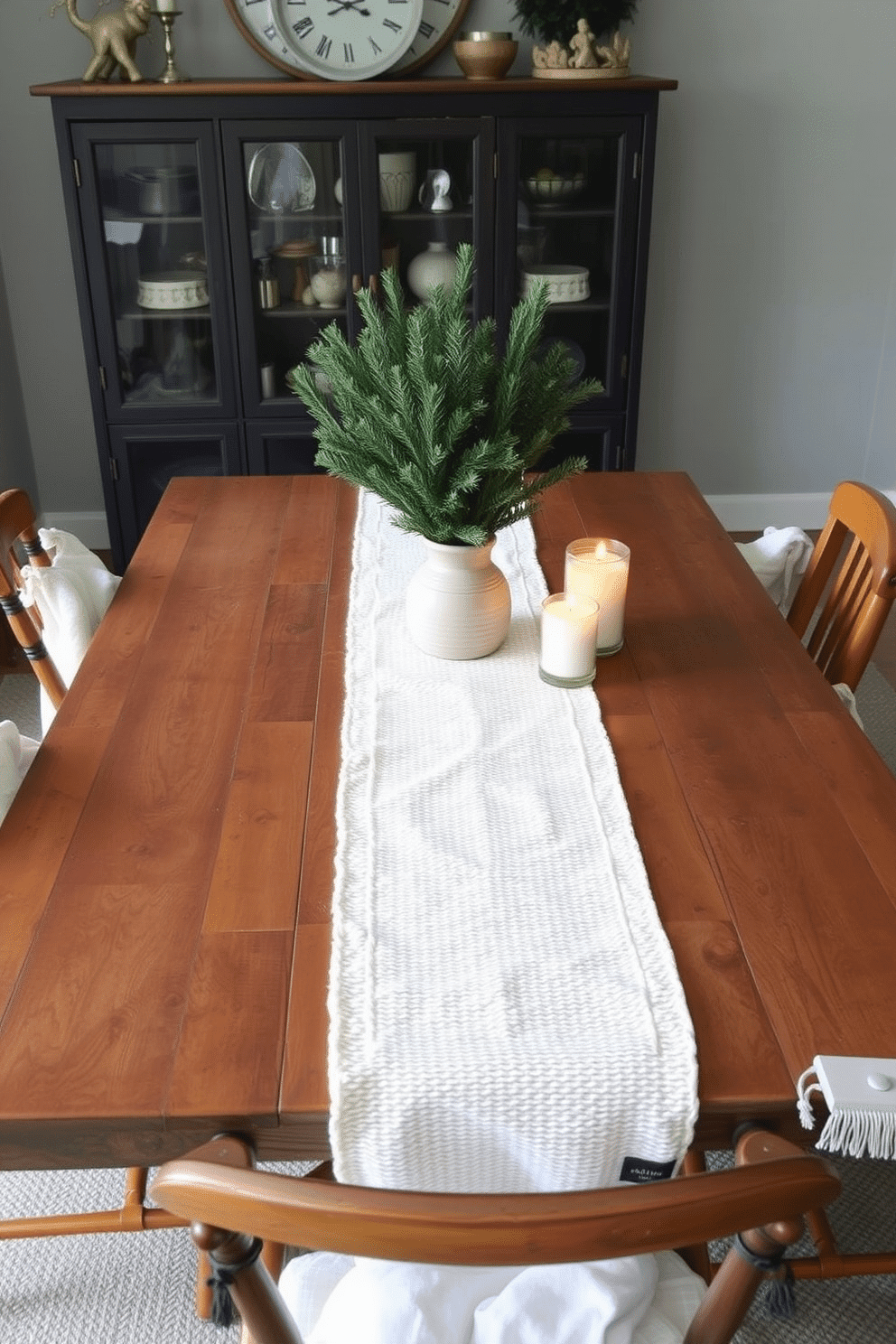 Create a cozy winter dining setting featuring a rustic wooden table adorned with a textured white table runner. Surround the table with mismatched chairs, each draped with a soft throw blanket for added warmth and style. In the center of the table, place a collection of evergreen branches in a simple ceramic vase. Add small decorative candles in varying heights to create a warm and inviting atmosphere.