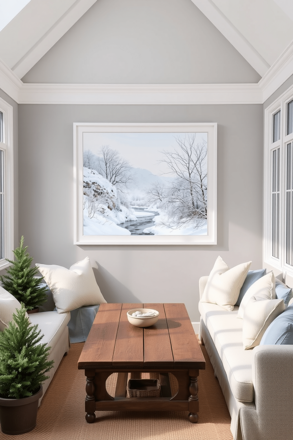 A serene winter landscape adorns the wall, showcasing snow-covered trees and a gentle stream under a soft blue sky. The artwork is framed in a simple white frame that complements the room's decor. The sunroom is filled with natural light, featuring cozy seating arranged around a rustic wooden coffee table. Plush cushions in shades of cream and pale blue enhance the inviting atmosphere, while potted evergreen plants add a touch of greenery.