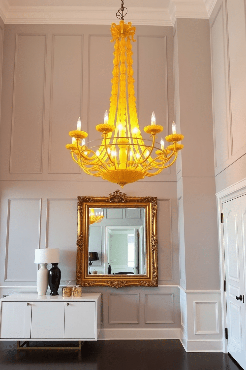 An elegant yellow chandelier hangs from a high ceiling, casting a warm glow over the spacious foyer. The walls are adorned with soft gray paneling, creating a sophisticated backdrop for the striking light fixture. The foyer features a sleek console table with a glossy white finish, topped with decorative items in complementary colors. A large mirror with an ornate gold frame reflects the chandelier's light, enhancing the room's brightness and elegance.